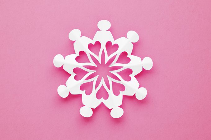 Chain Of Volunteer People Made of Paper creating a snowflake-like pattern on Pink Background