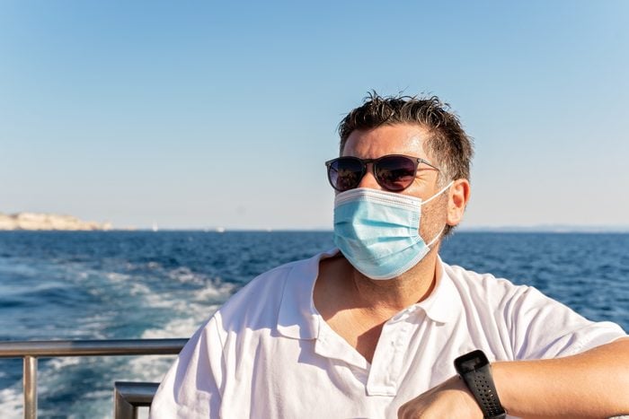 Portrait of man wearing face mask traveling on boat in the sea at summer holidays during coronavirus pandemic. New normal. Tourist in sunglasses having boat trip tour on vacation.