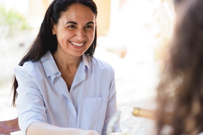 Friend smiling while looking at woman pouring wine in glass at back yard