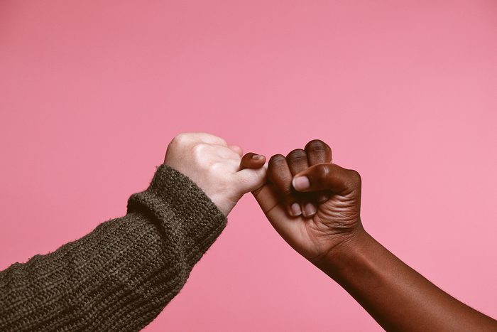 Studio shot of two young women linking their fingers against a pink background