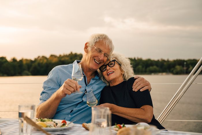 Happy senior man with arm around woman having wine against sea in boat