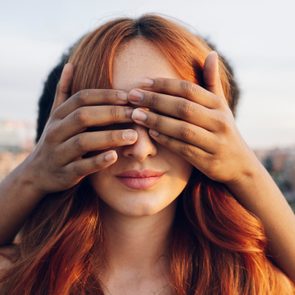 Woman covering eyes of redhead girlfriend with hands at sunset