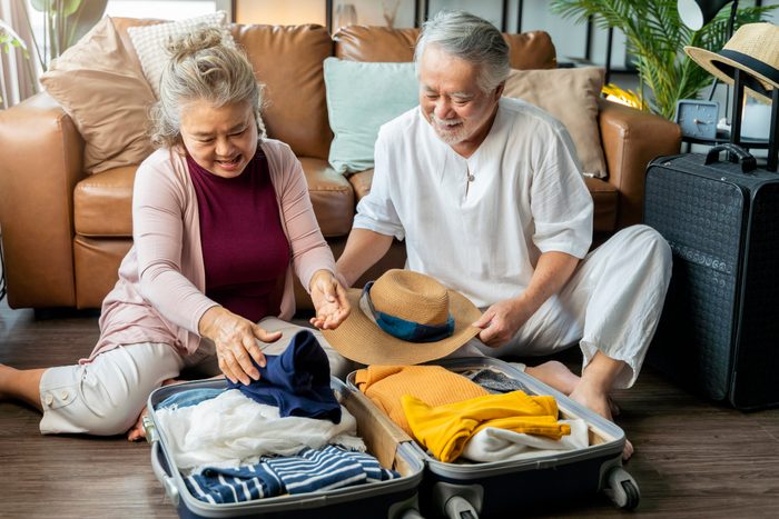 old asian senior couple packing cloth and stuff for a trip together,happiness asian old age retired mature adult enjoy arrange cloth together on floor at living room at home interior background