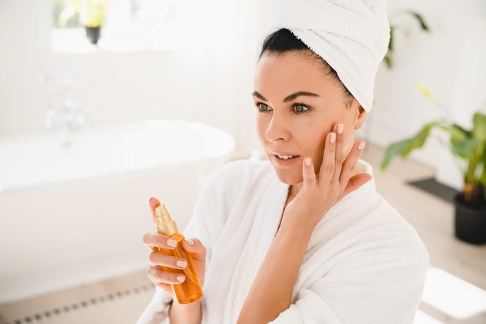 Pretty caucasian middle-aged mature woman in turban and spa bathrobe applying beauty rejuvenation oil product on her face for anti-age anti-wrinkle effect