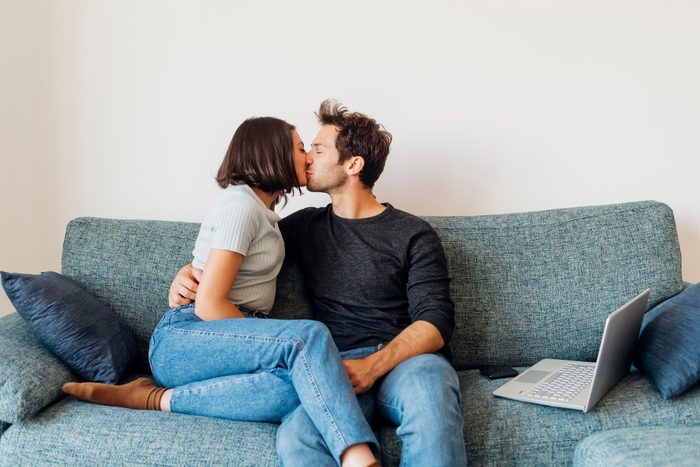 Affectionate young couple kissing with eyes closed on sofa at home