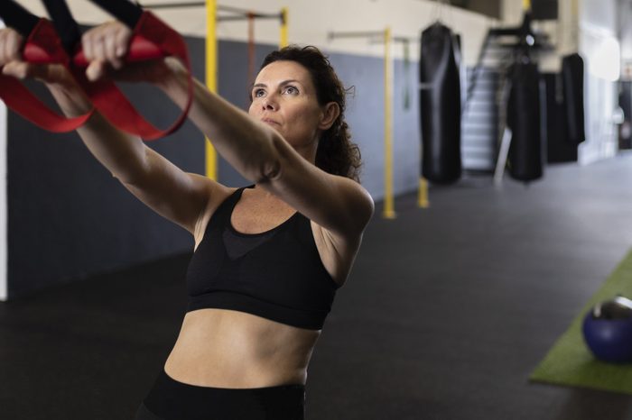 Sportswoman leaning backwards pulling straps in gym