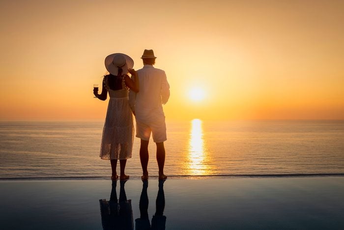 A couple stands by the swimming pool and enjoys the sunset over the mediterranean sea