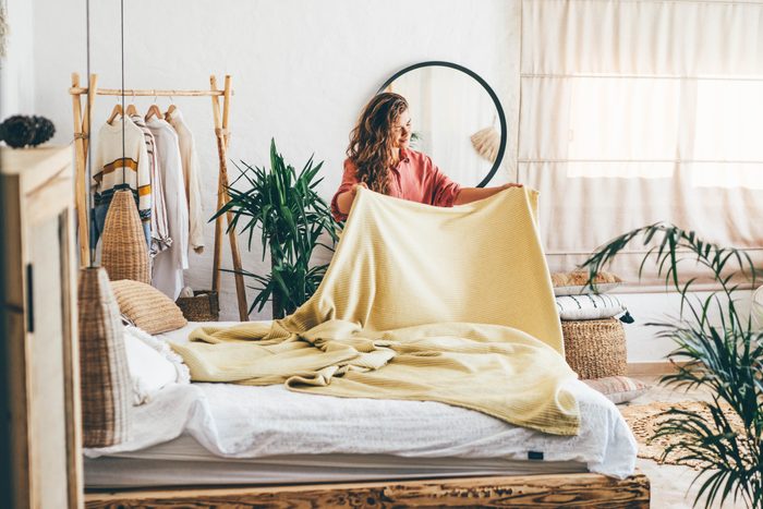Woman doing her morning routine, arranging pillows and making up bed at home.