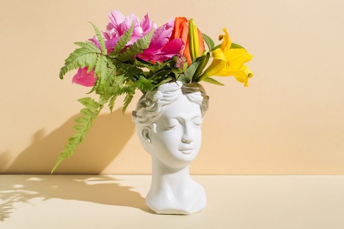 head sculpture vase with closed eyes with flowers on beige background.