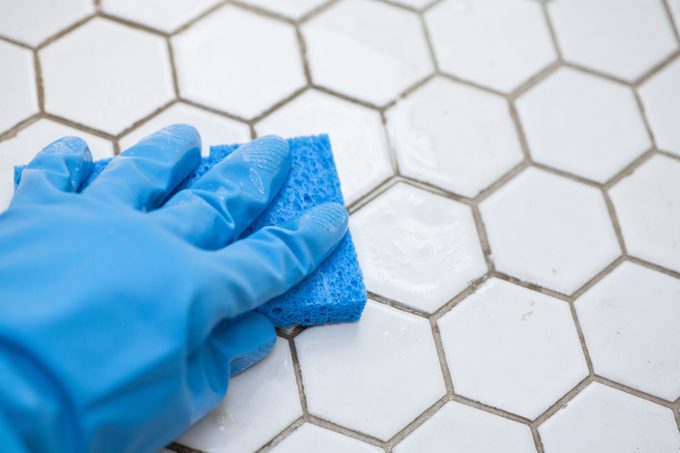 blue cleaning gloves holding a sponge cleaning a tile floor