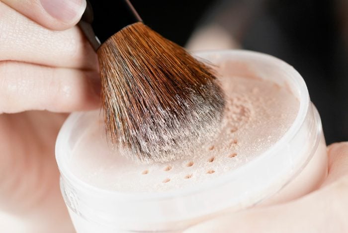 Close-up of a woman's hand holding a pot of face powder and a make-up brush