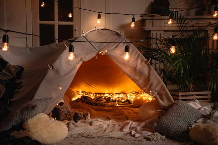 handmade tent with blankets, pillows, toys and lights in room