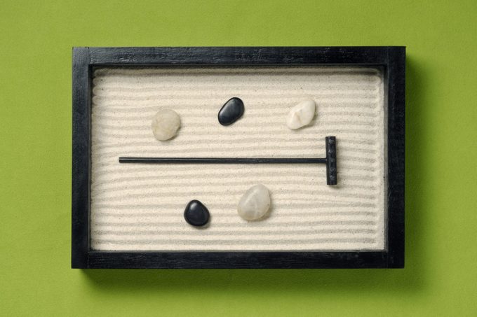 A small wooden zen garden with rocks and a small black rake on green background