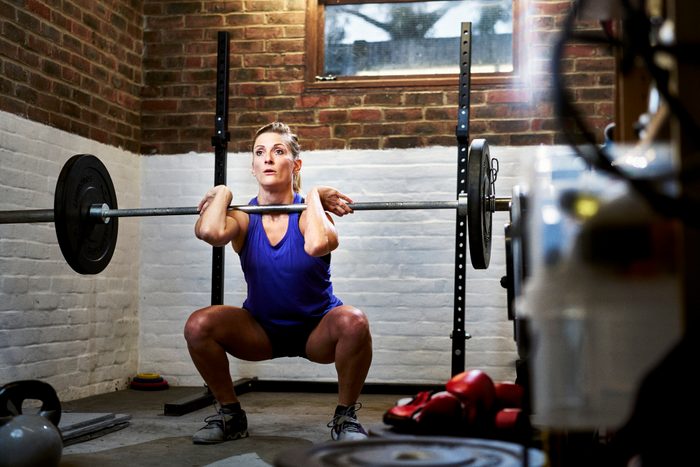 Woman exercising in home gym in converted garage performing a squat or clean