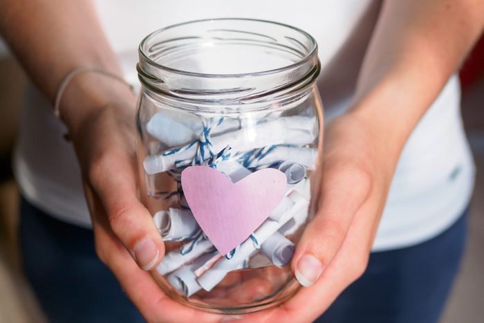 Woman holds a jar with pink heart and curled notes in her hands