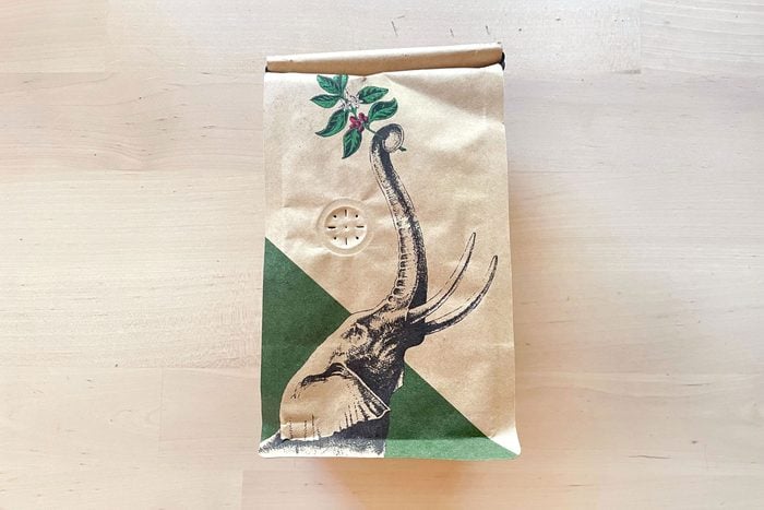 a hole in a brown coffee bag with an elephant illustration on it, resting on a light colored wooden table