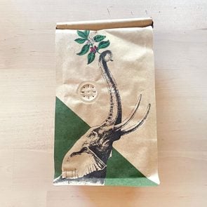a hole in a brown coffee bag with an elephant illustration on it, resting on a light colored wooden table