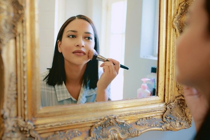 woman looking in a mirror and applying setting powder with a fluffy brush