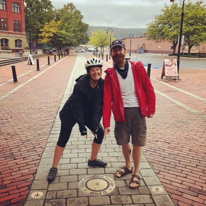 husband and wife posing in the middle of a brick pathway in a town