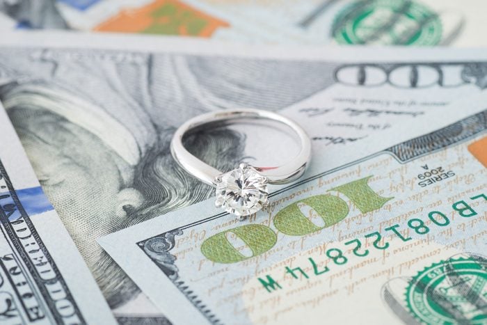 a diamond engagement ring sitting atop some scattered hundred dollar bills