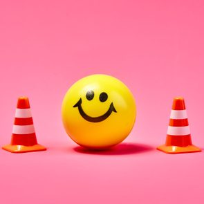 a yellow smiley face ball between two traffic boundary cones on pink background