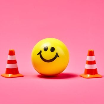 a yellow smiley face ball between two traffic boundary cones on pink background