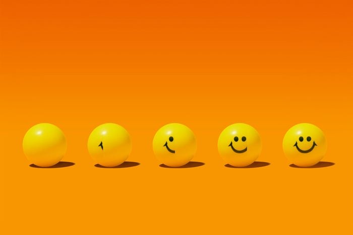 five yellow balls on an orange background; from left to right, the smiley face is more revealed to symbolize practicing gratitude to increase happiness