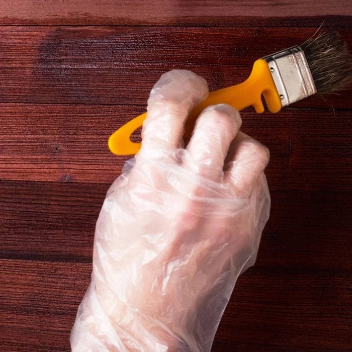 Yellow brush painting a new coat of finish on a dark hardwood background