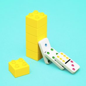 a yellow toy brick tower remains standing as three dominoes fall towards it