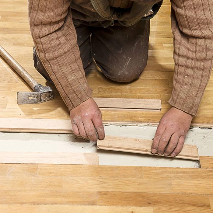 Man replacing a section of his hardwood floors with new planks for a home renovation