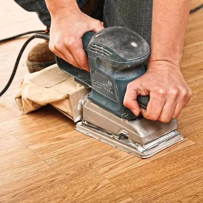 Man using a sander on the hardwood floors to fix the imperfections in his house