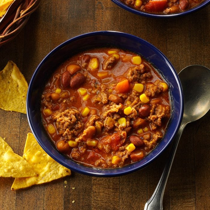 Simple Taco Soup in a blue bowl on dark wood background with soup spoon and tortilla chips nearby