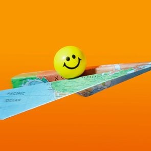 Smiley yellow ball riding On A Paper Airplane made from a map; orange background