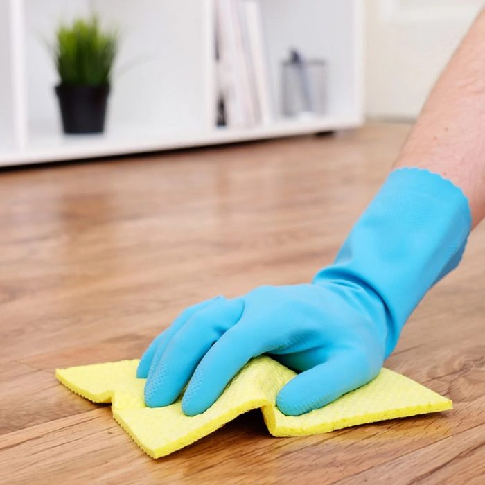 Cleaning the wood floors with a thin yellow sponge and glove