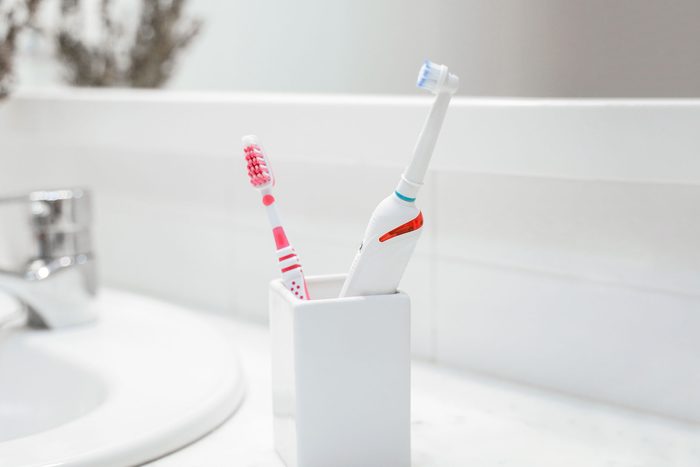 a manual toothbrush and an electric toothbrush in a cup next to a sink in a clean white bathroom