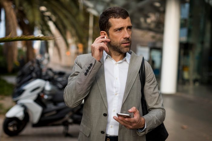 Businessman with cell phone in the city applying earbuds