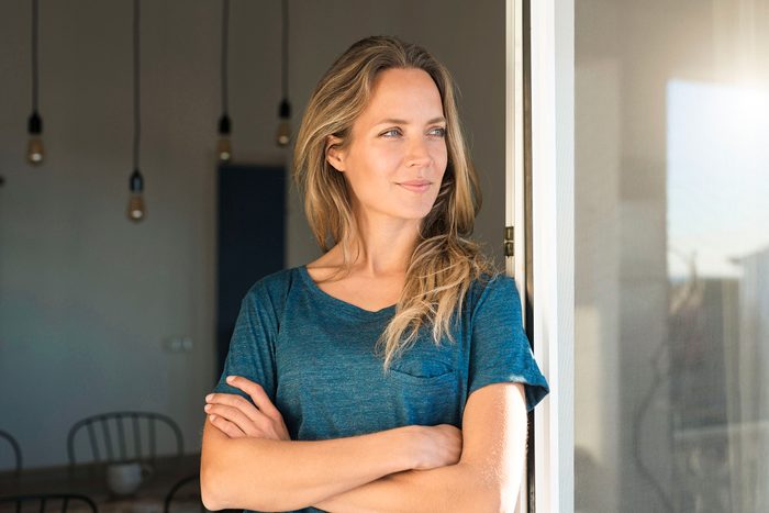 Woman leaning at open window at home looking sideways