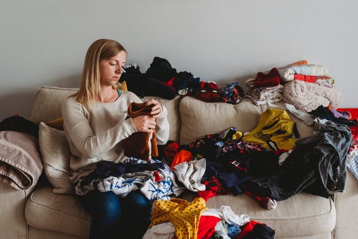 Woman folding large pile of laundry on sofa at home