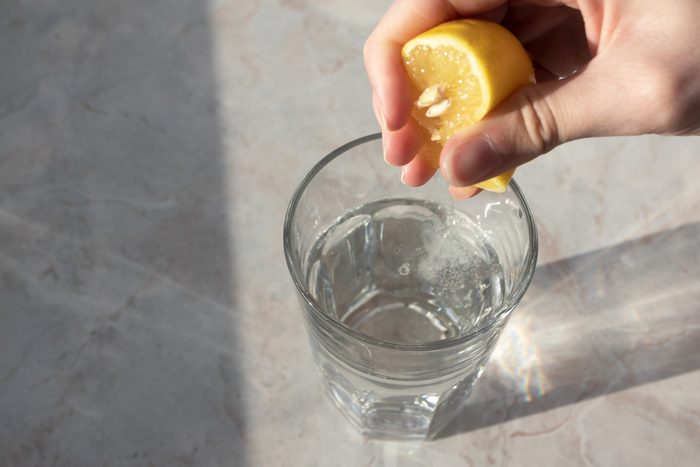 Hand squeezes lemon juice in glass with soda water on marble table background. Detox healthy drink concept
