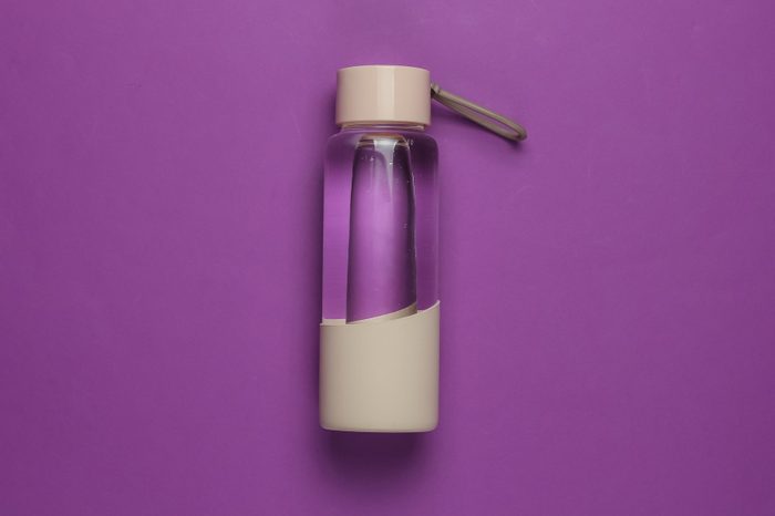 Bottle of water for sports and outdoor activities on purple background. Top view