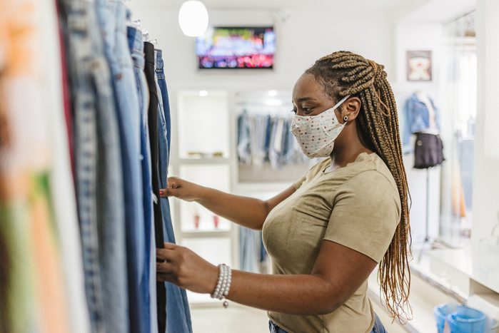 Woman customer choosing clothes at the mall store while wearing a face mask