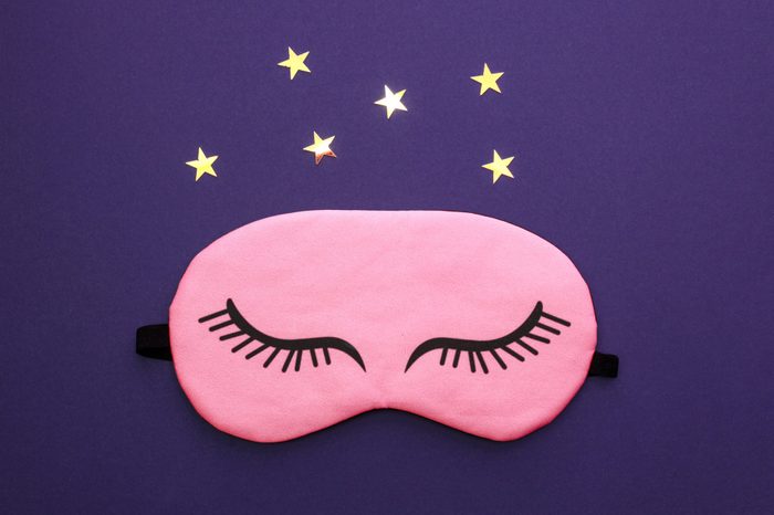 Pink sleep mask over dark purple background. Concept of sleep, health care and daily routine.