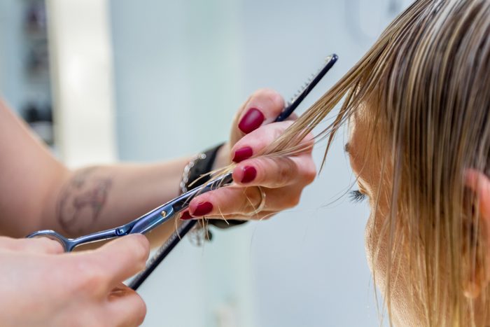 Hands of a professional hairdresser scissors the bangs of wet hair of a blonde woman. Fashionable hairstyle design in a beauty salon. Small female business