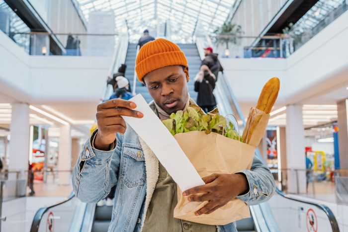 Surprised African American man looks at receipt total with food in mall