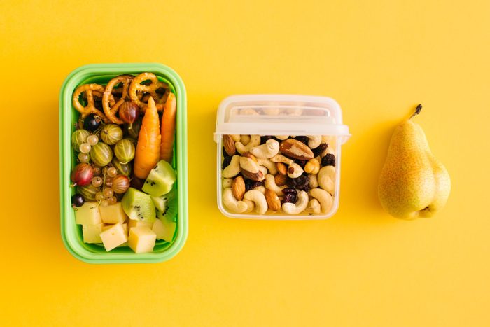 Open lunch box with healthy lunch delicious food, fruits, berries, vegetables, snacks and nuts on yellow background. Concept of school nutrition. Flat lay, top view