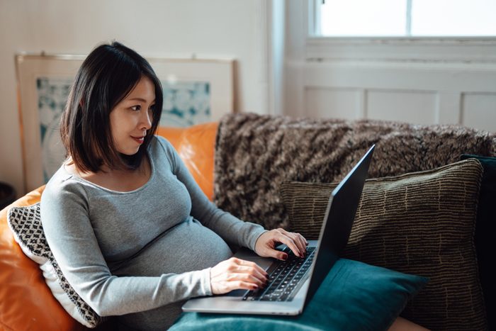 Young pregnant businesswoman at home office, working with laptop on sofa
