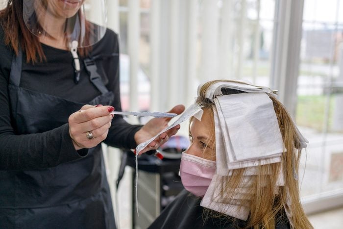 Hairdresser hair coloring customer's hair and wearing visor