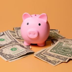 A piggy bank with US dollar bills isolated on an orange color background in studio photo. Finance and economy concept.