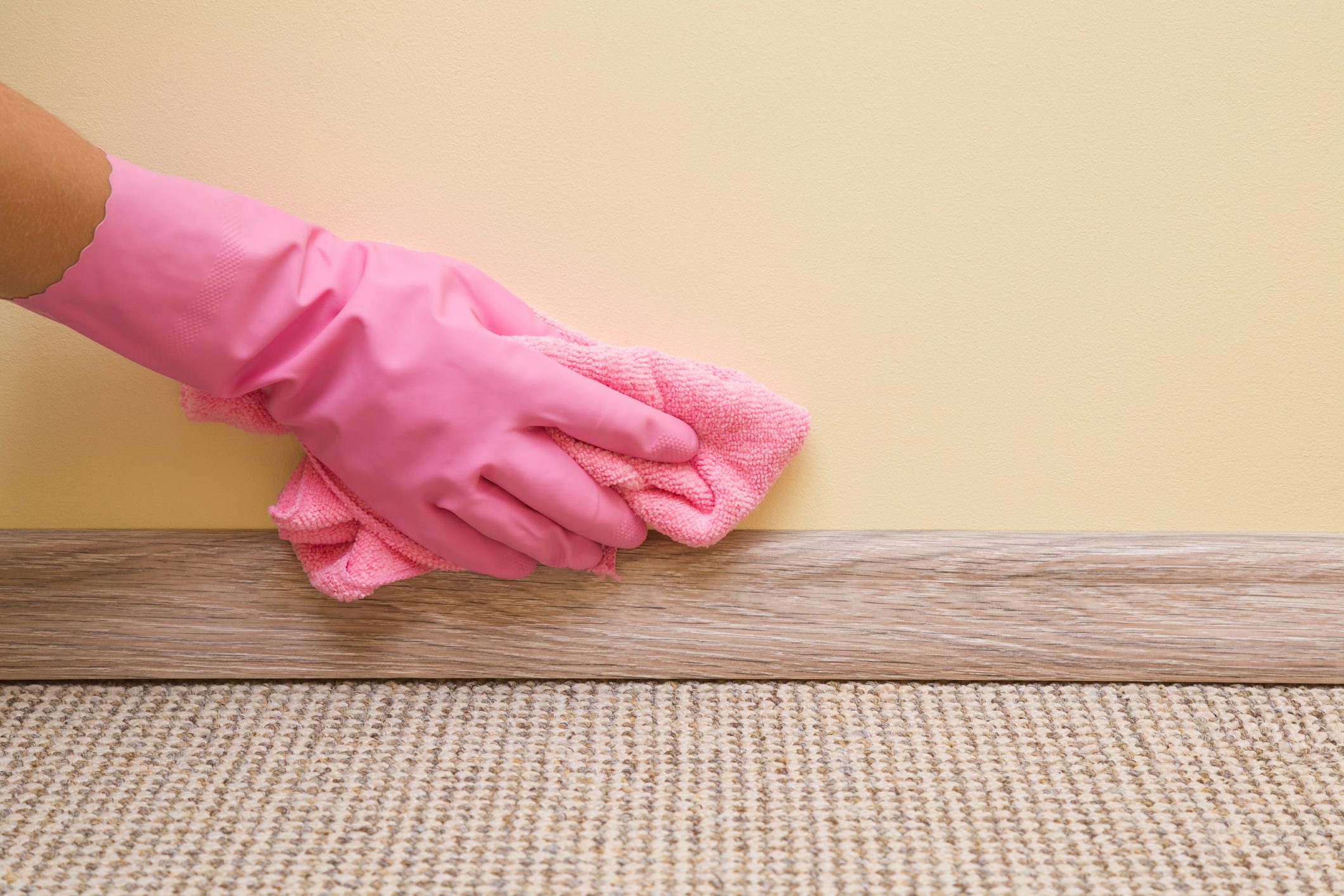 Hand in rubber protective glove with microfiber cloth cleaning baseboard on the floor from dust at the wall. Early spring cleaning or regular clean up. Maid cleans house.