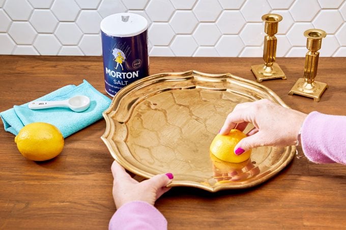 hands cleaning a brass tray with a cut lemon